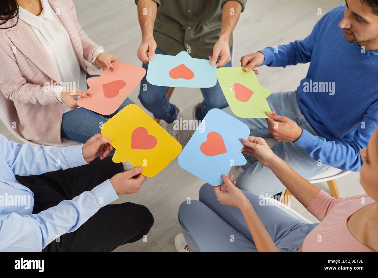 Young people sitting in circle and holding colored speech bubbles with red hearts on them. Stock Photo