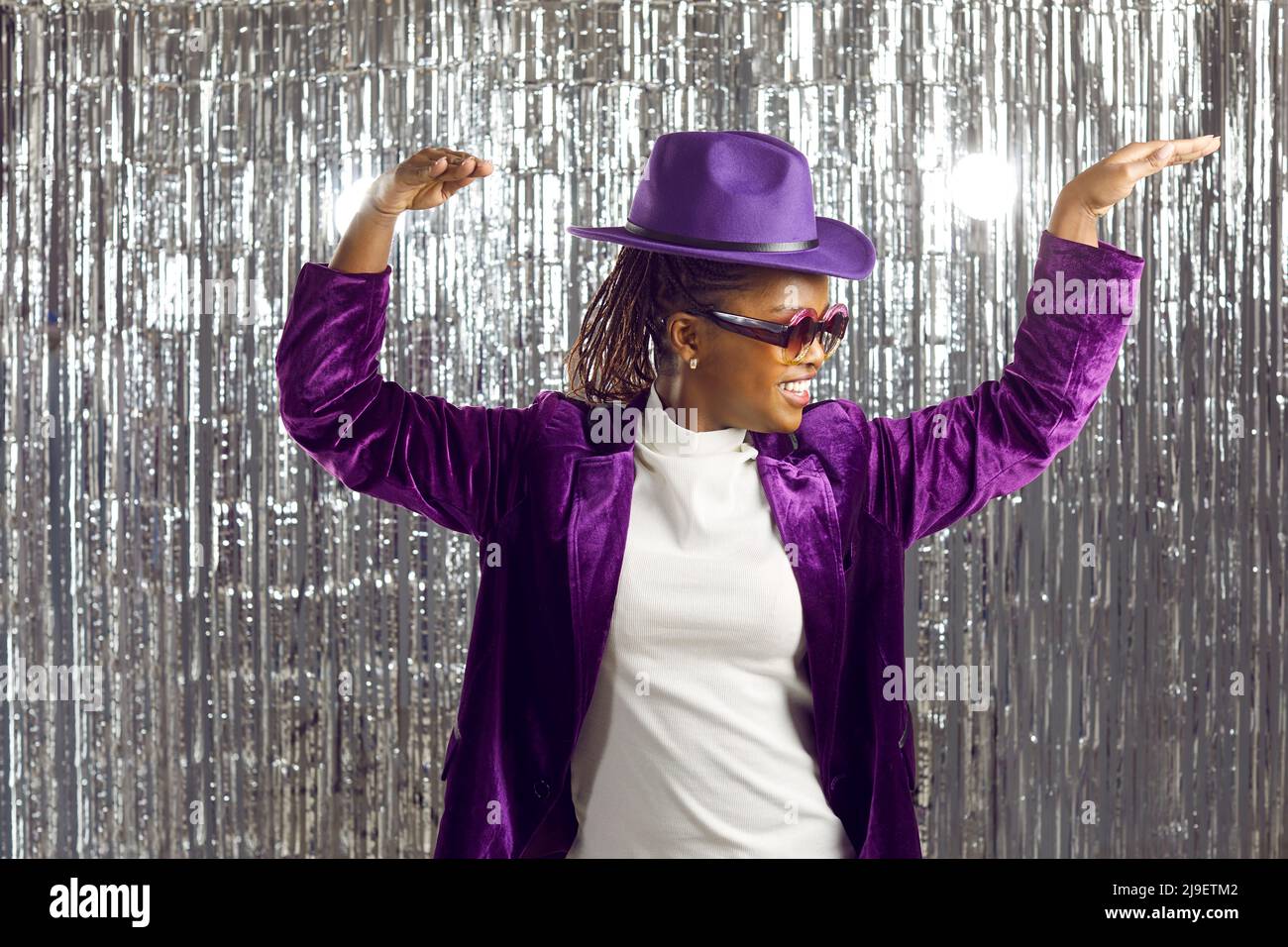 Happy Black woman in a purple hat and disco glasses dancing and having fun at a party Stock Photo