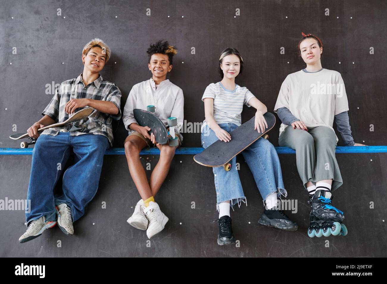 Minimal shot of diverse group of teenagers looking at camera while sitting on ramp in skateboarding park Stock Photo