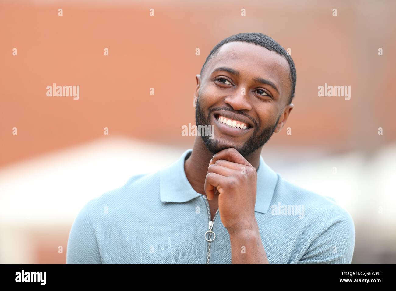 Front view portrait of a happy man with black skin thinking looking at side in the street Stock Photo