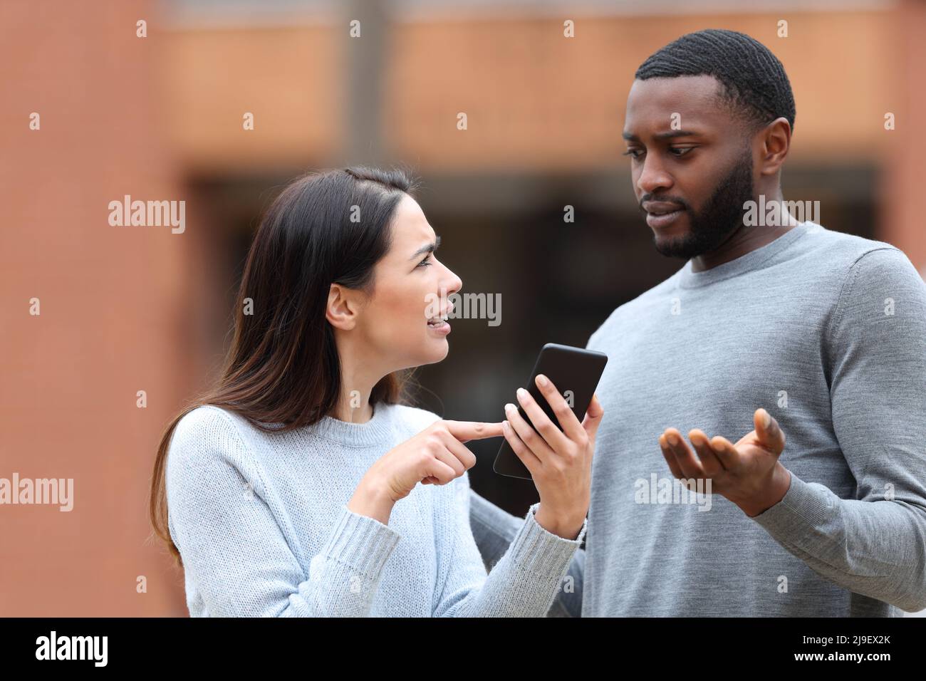 Disgusted woman asking for explanation about mobile phone text to a man in the street Stock Photo