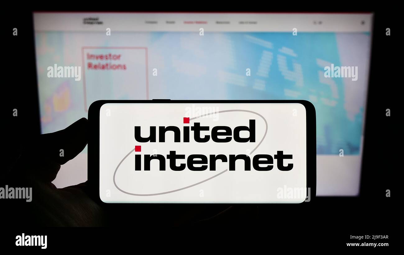 Person holding cellphone with logo of German company United Internet AG on screen in front of business webpage. Focus on phone display. Stock Photo