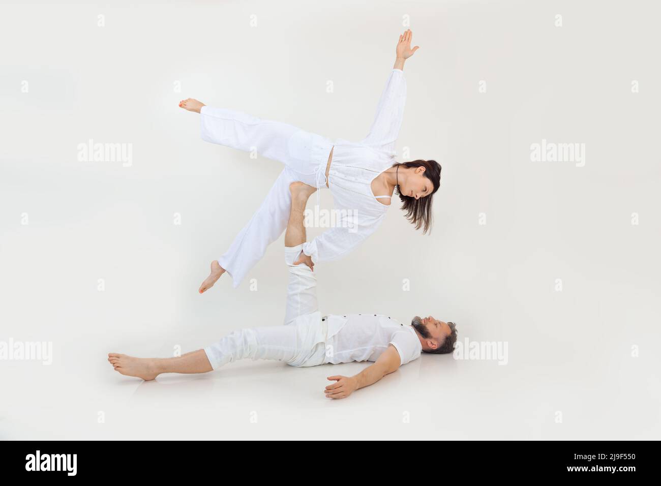 Man and woman, family do sport exercises, fitness and acrobatics yoga. Spirituality and zen meditation. Holding on leg Stock Photo