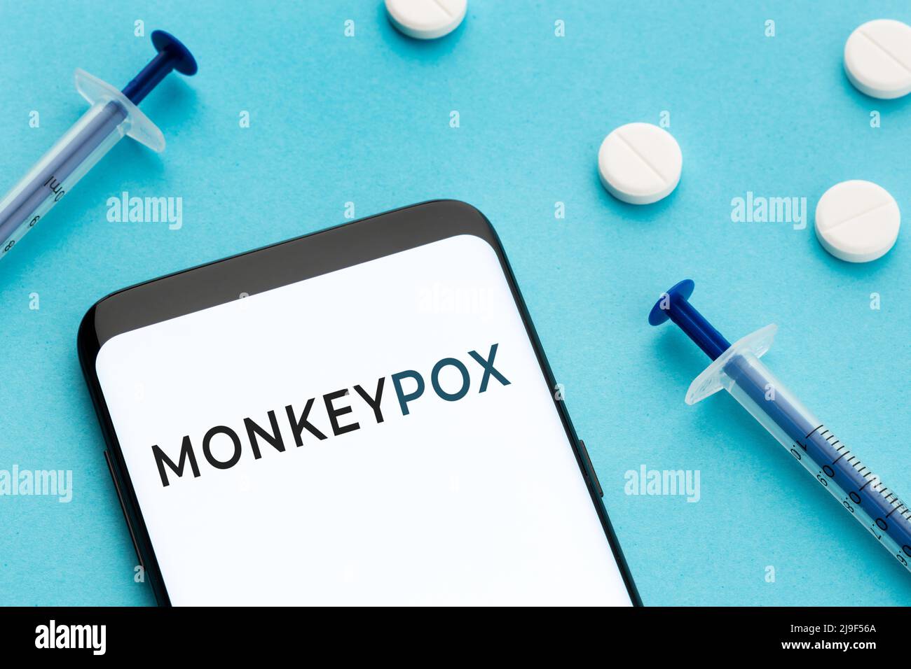 Samrtphone with text Monkeypox pills and syringes on blue background Stock Photo