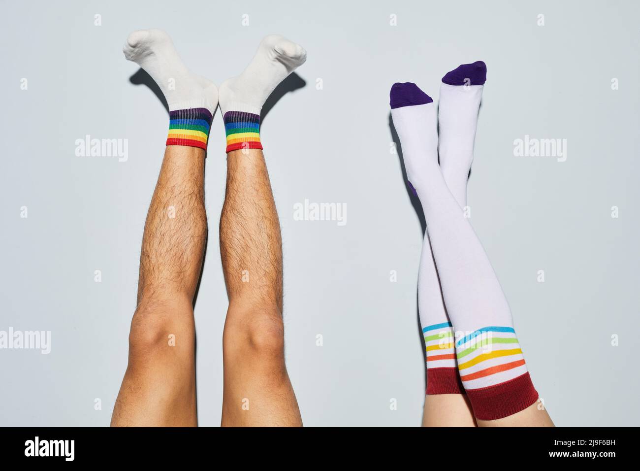 Minimal shot of playful young couple wearing socks with rainbow symbols feet up against white wall Stock Photo