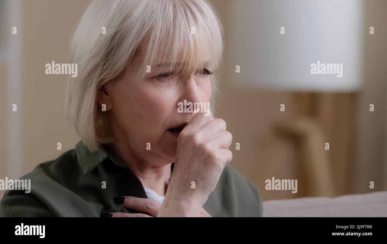 Portrait old woman coughing at home. Close up unwell Caucasian aging mature lady coughs having pain in chest coronavirus symptoms. Grandmother suffer Stock Photo