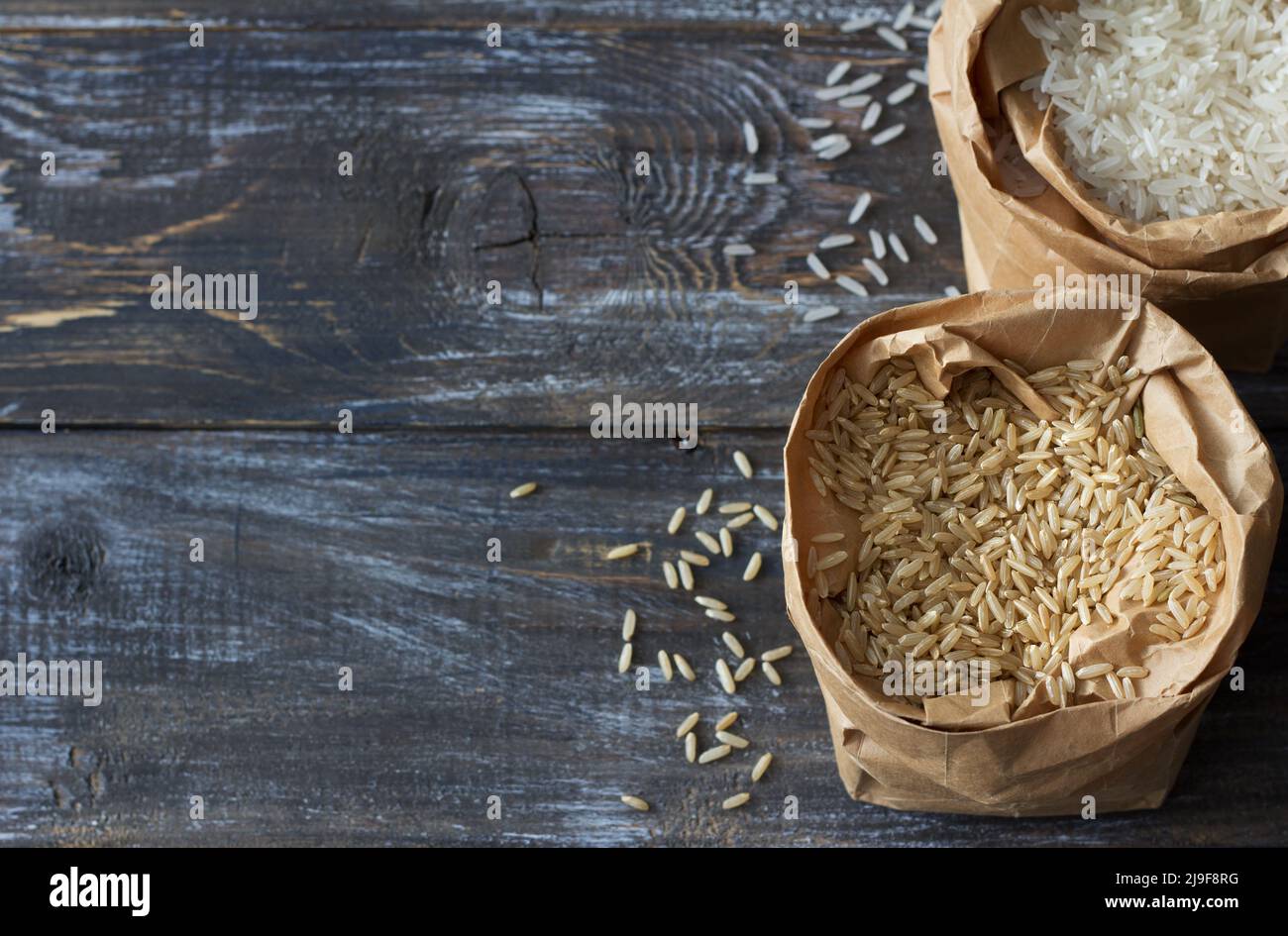 Raw long-grain brown and white basmati  rice in a paper craft bags on a wooden background, space Stock Photo