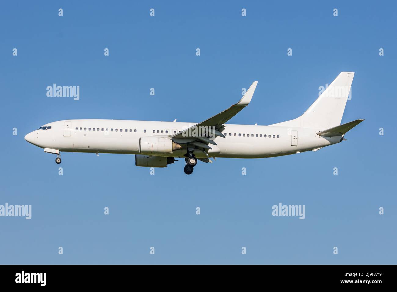 Afull white neutralized Boeing 737 airplane landing with blue skies, usable as a template for liveries. Stock Photo
