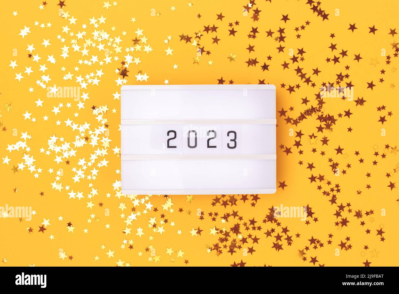 Lightbox with 2023 numbers on a yellow background with golden stars confetti. Stock Photo