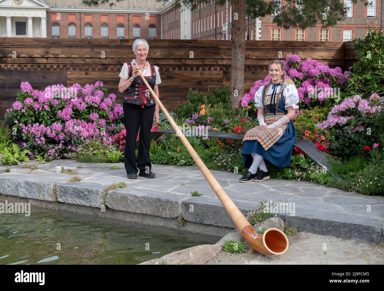 Royal Hospital, Chelsea, London, UK. 23 May 2022. The RHS Chelsea Flower show opens to the press back in it’s normal early Summer slot running from 24-28 May. Image: A Swiss Sanctuary Show Garden with Alpenhorn player dressed in traditional swiss attire. Credit: Malcolm Park/Alamy Live News. Stock Photo