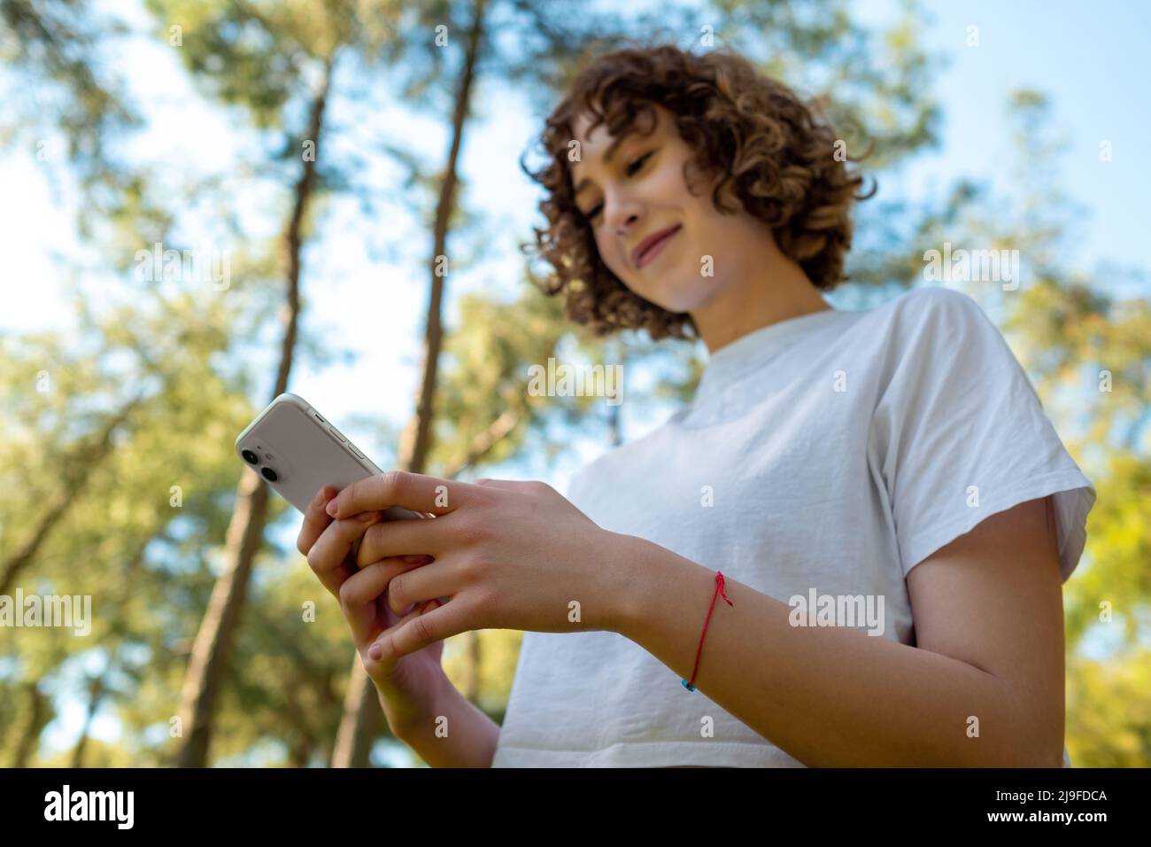 Bottom view of young redhead woman using phone or watching video or  messaging with friends with big smiles while standing on city park,  outdoors Stock Photo - Alamy