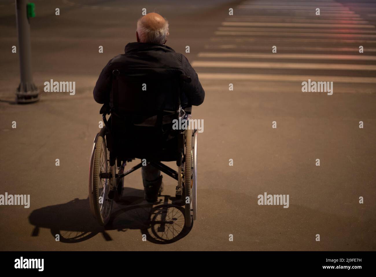 Wheelchair accessible at night. Man in wheelchair for disabled on road. Accessible environment in city. Person with disabilities. Medical chair. Stock Photo