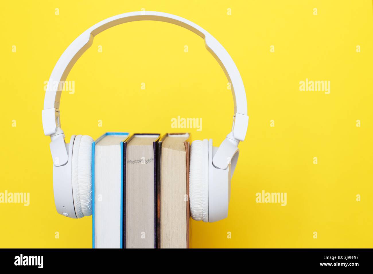 Audio book concept with modern white headphones and hardcover book on a yellow background. Listening to a book. E-learning. Copyspace. Stock Photo