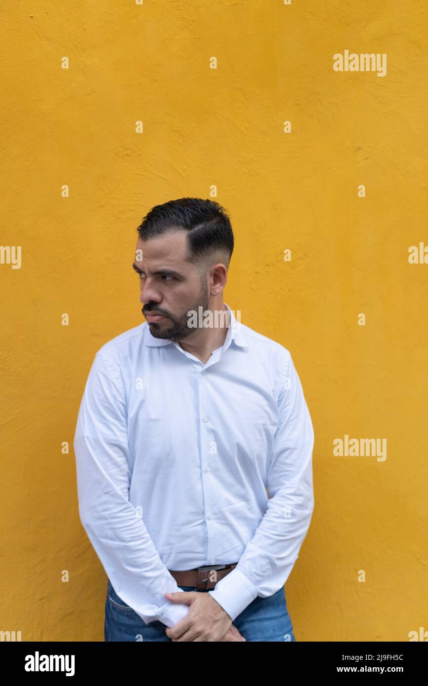 Young man standing in front of a yellow wall. He is looking to the side with seriousness Stock Photo
