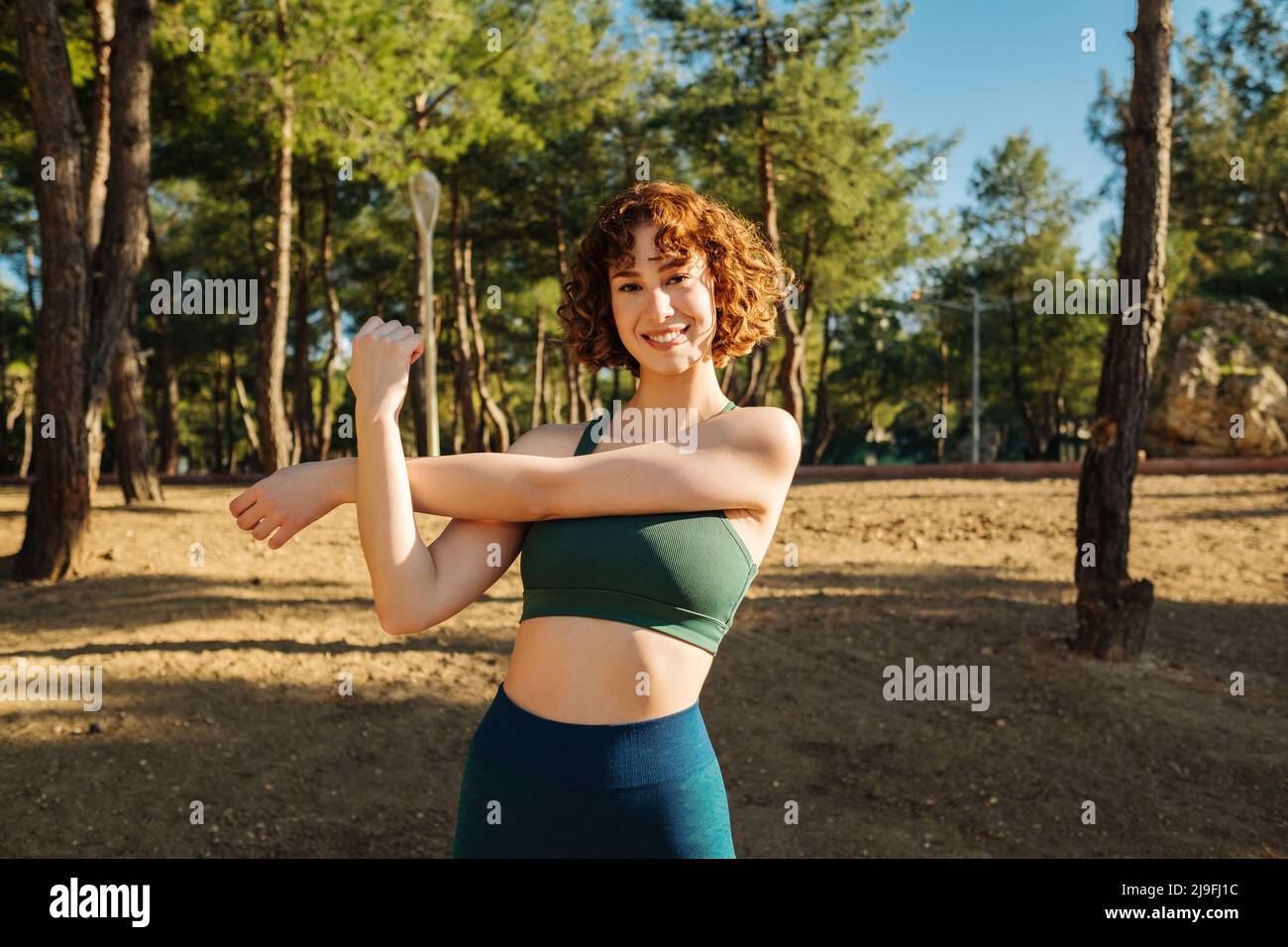 Happy sportive redhead woman wearing sports bra and blue yoga pants
