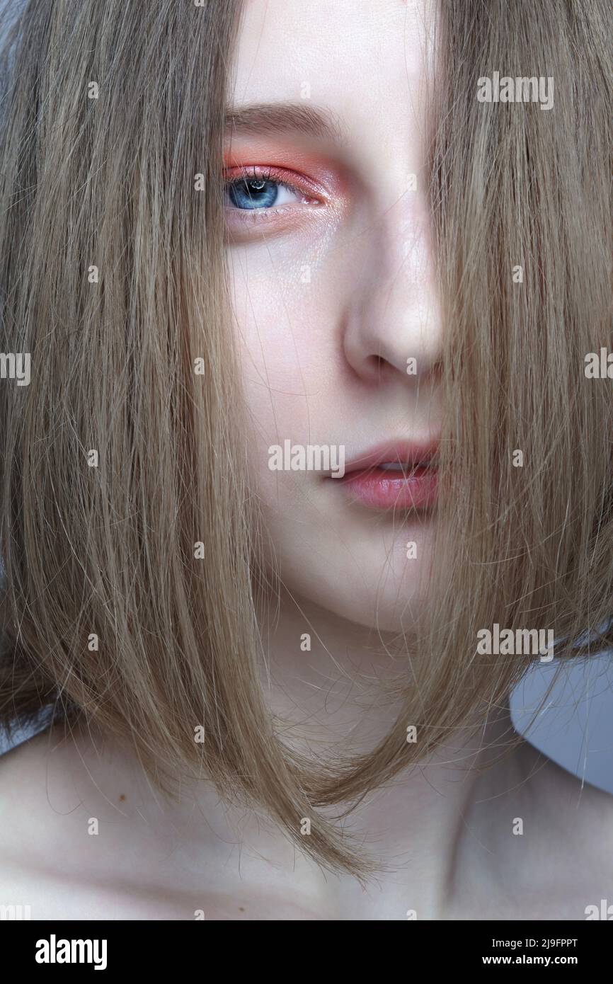 Close-up portrait of beautiful  young woman. Female with blond hair covering her face looks at the camera. Stock Photo