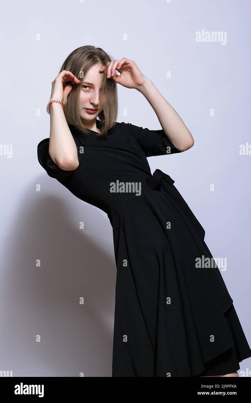 Portrait of beautiful blonde female in black dress. Young woman posing on white background. Stock Photo
