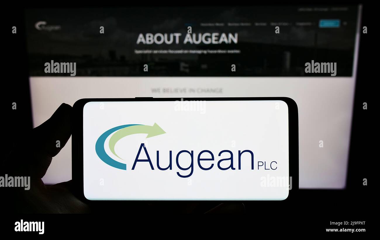 Person holding smartphone with logo of British waste management company Augean plc on screen in front of website. Focus on phone display. Stock Photo