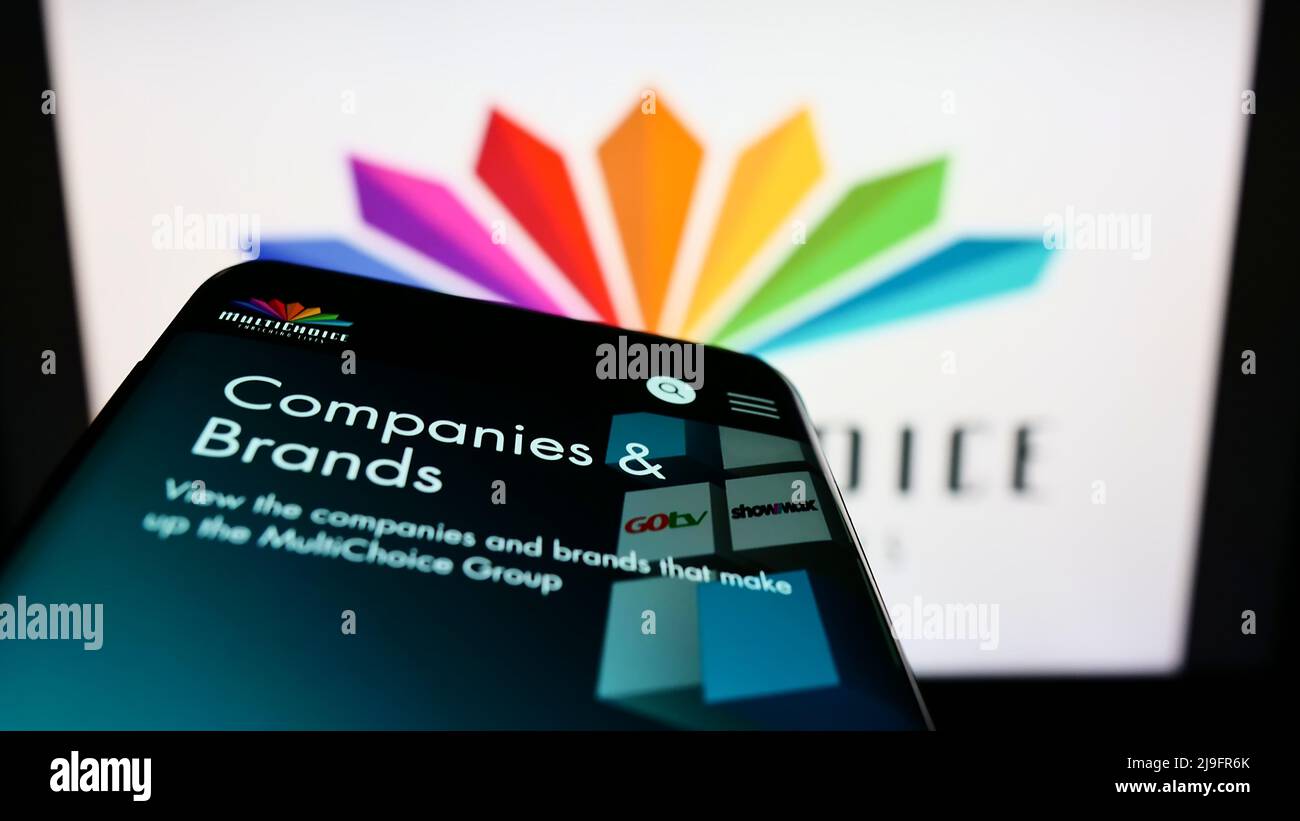 Mobile phone with webpage of South African media company MultiChoice Group on screen in front of logo. Focus on top-left of phone display. Stock Photo