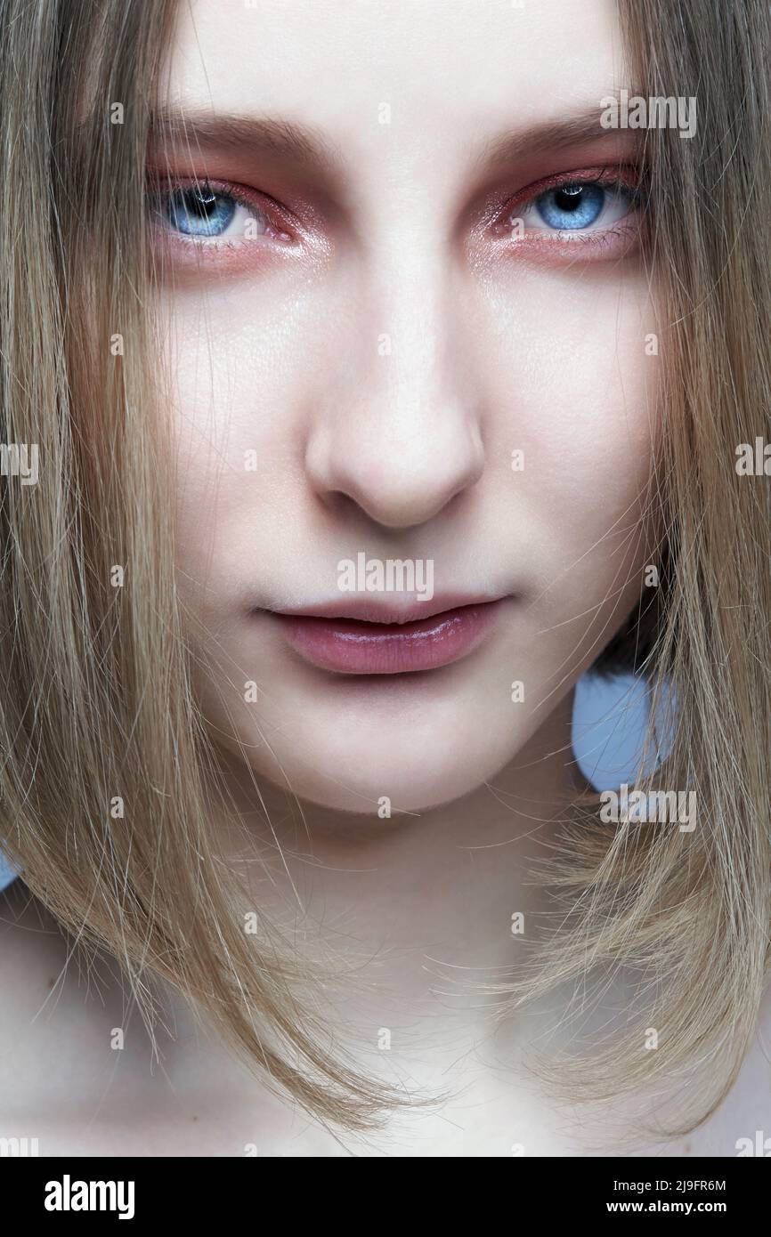 Close-up portrait of beautiful young woman. Female with blond hair covering her face looks at the camera. Stock Photo