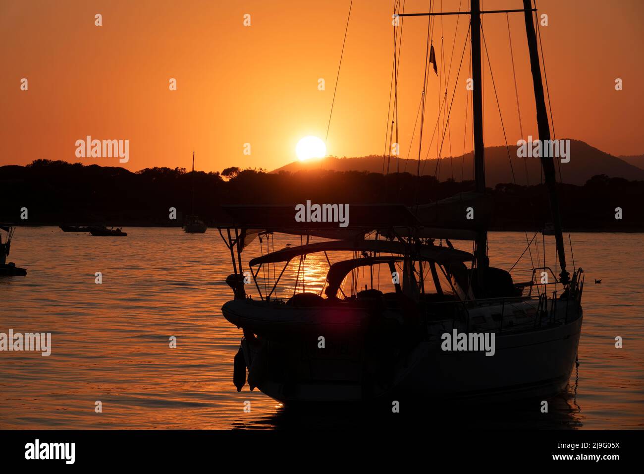A white sailboat sails on the sea with an orange sunset Stock Photo