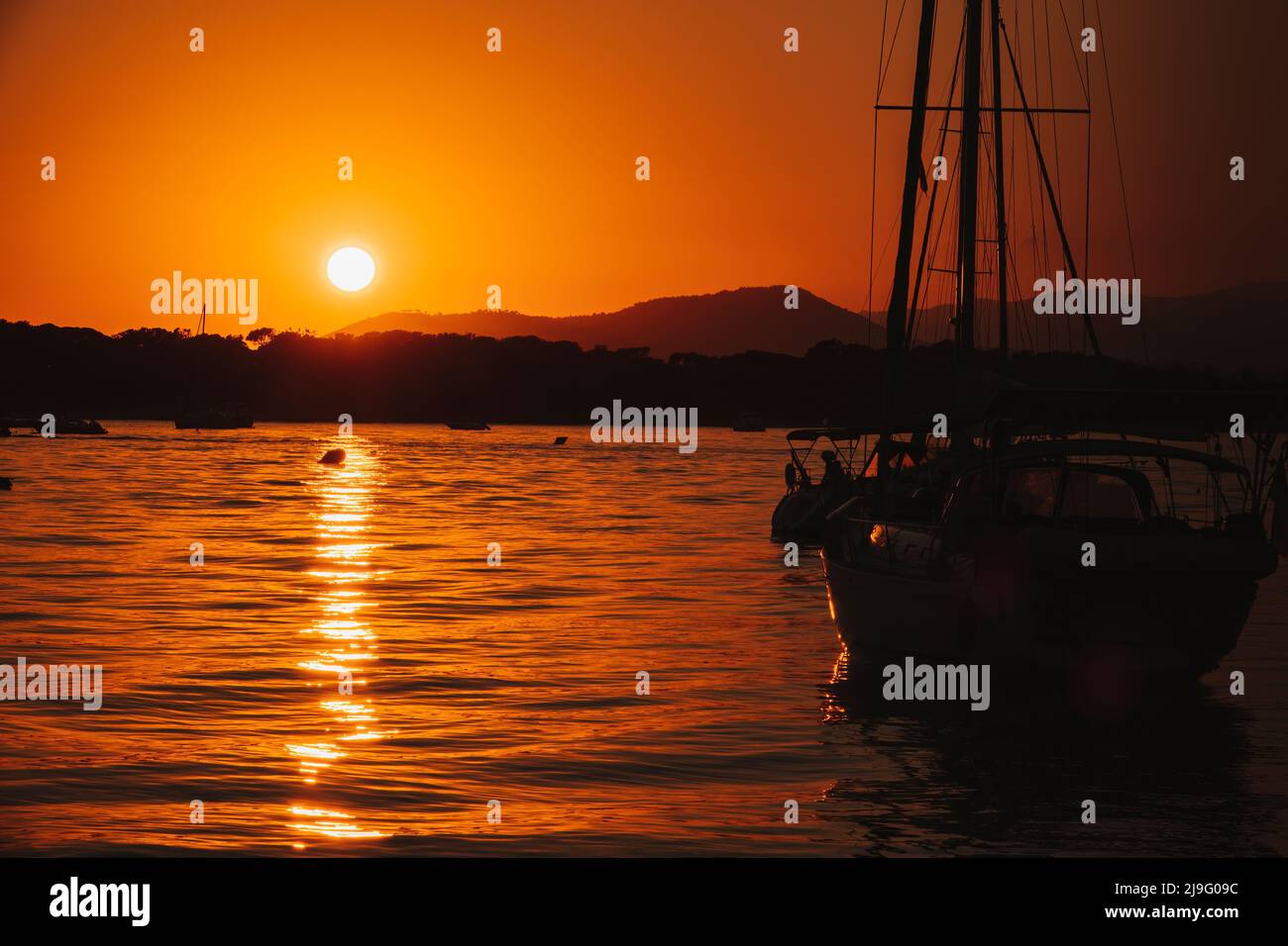 A white sailboat sails on the sea with an orange sunset Stock Photo