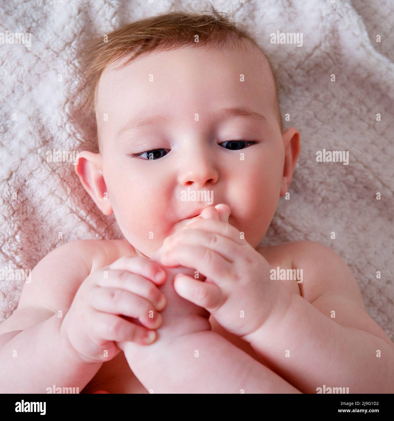 Portrait of a happy infant baby on the bed pulling his leg into his