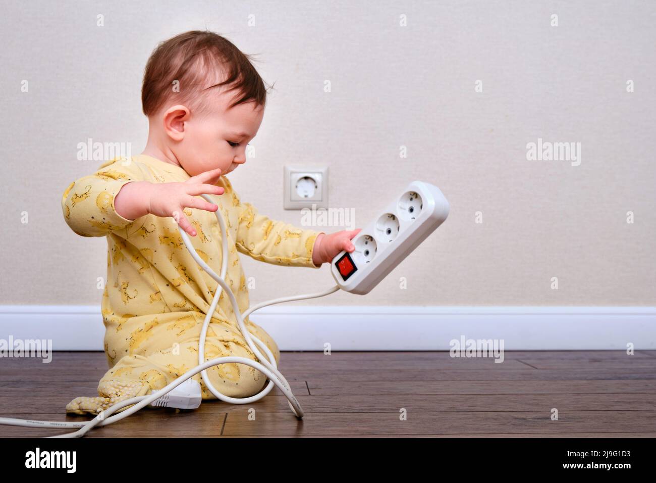 Toddler baby boy plays with electric wires while sitting on the floor