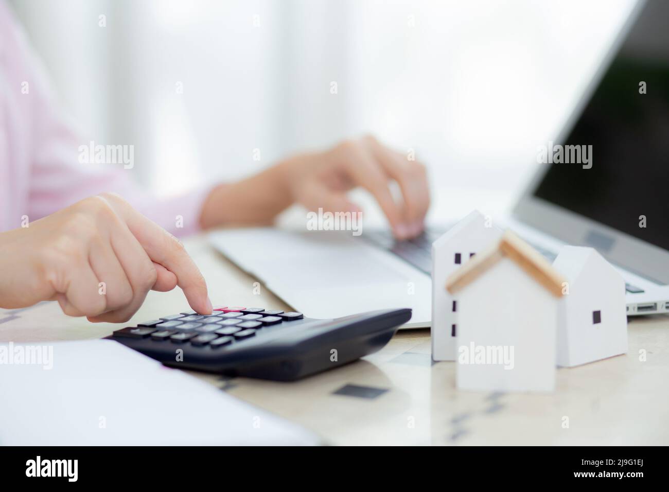 Closeup hands of woman sitting and planning and calculate expense and mortgage with calculator and home on desk, insurance and budget of residential, Stock Photo