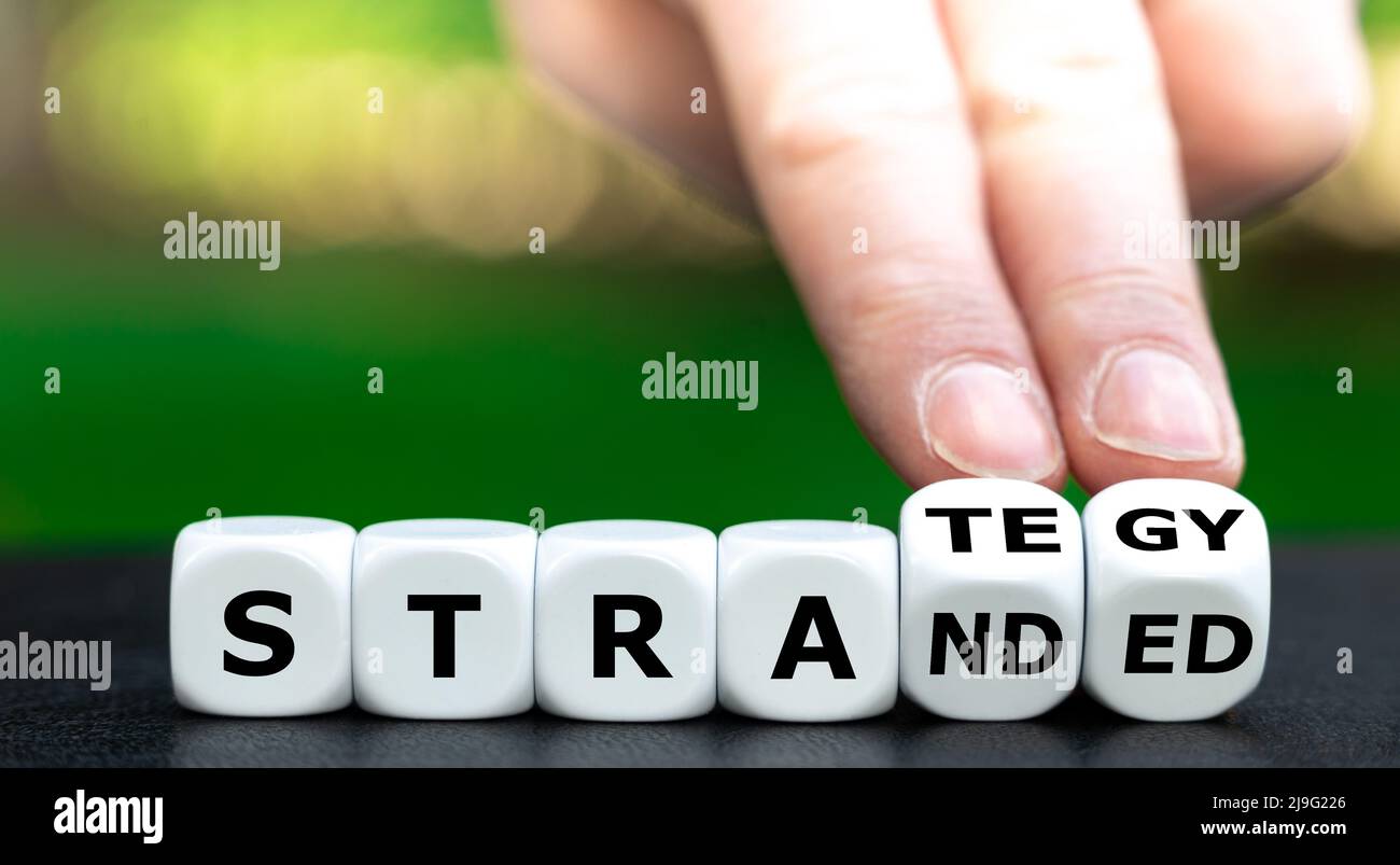 Hand turns dice and changes the word stranded to strategy. Stock Photo