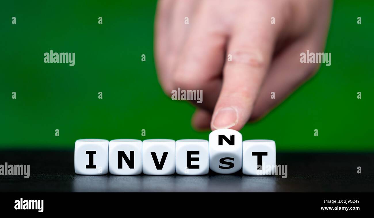 Hand turns dice and changes the word invest to invent. Stock Photo