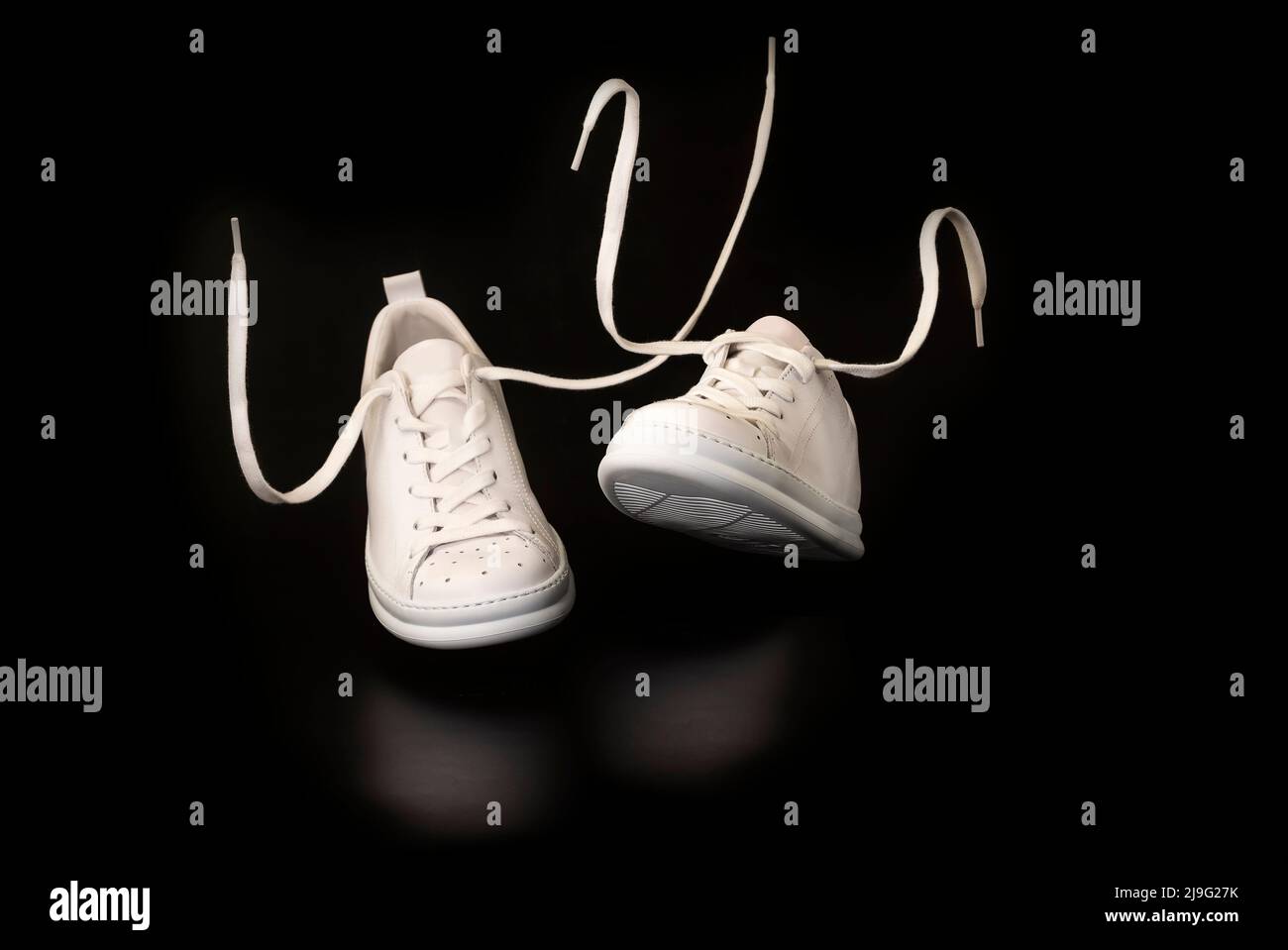 New Unbranded Stylish white sneakers or tennis shoes flying on black background shot with studio lighting. New Unbranded Sneakers or trainers on black Stock Photo