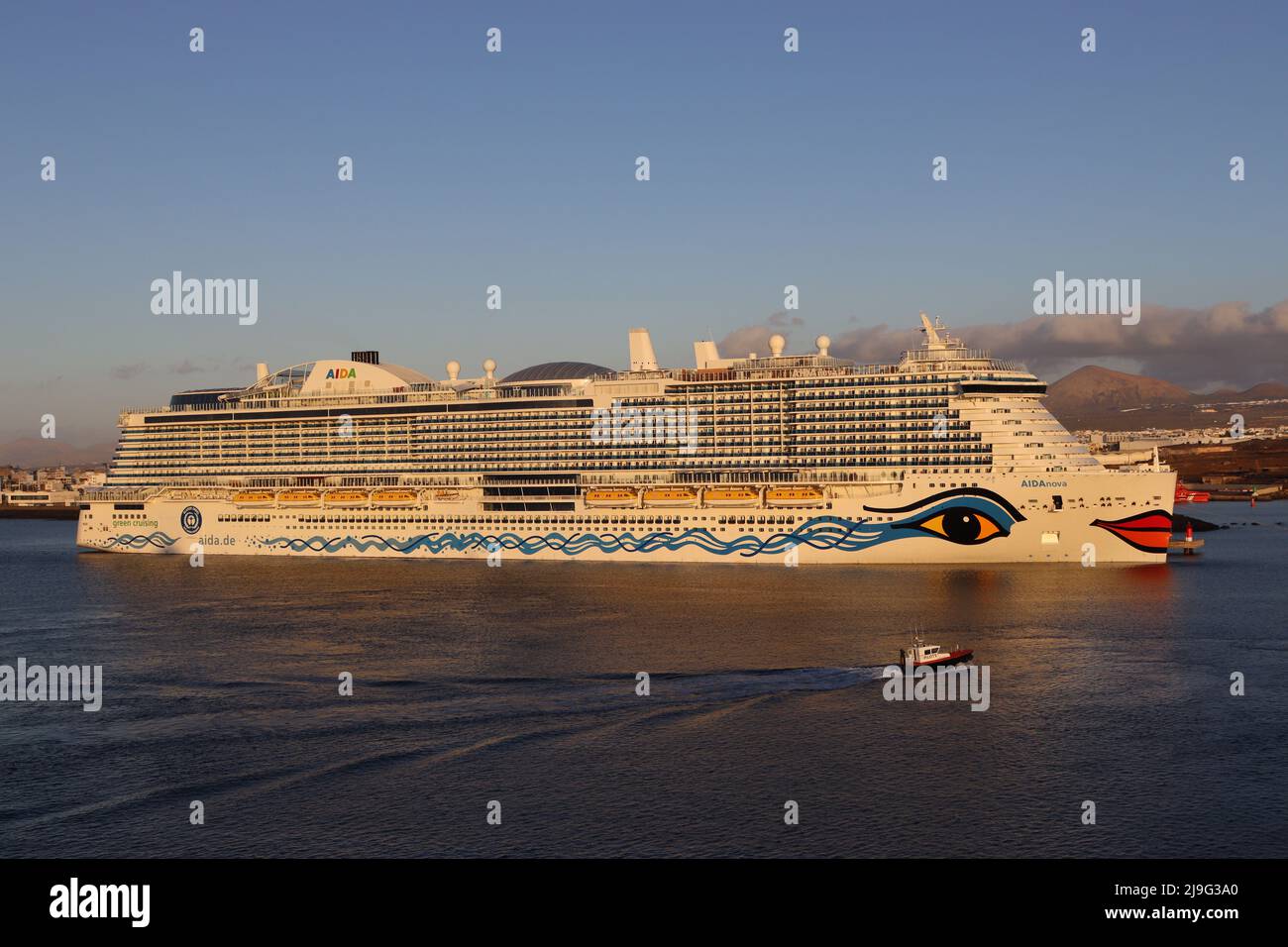 A Pilot boat is dwarfed by the 184,000  ton German cruise ship AIDAnova bathed in early morning sunlight Stock Photo