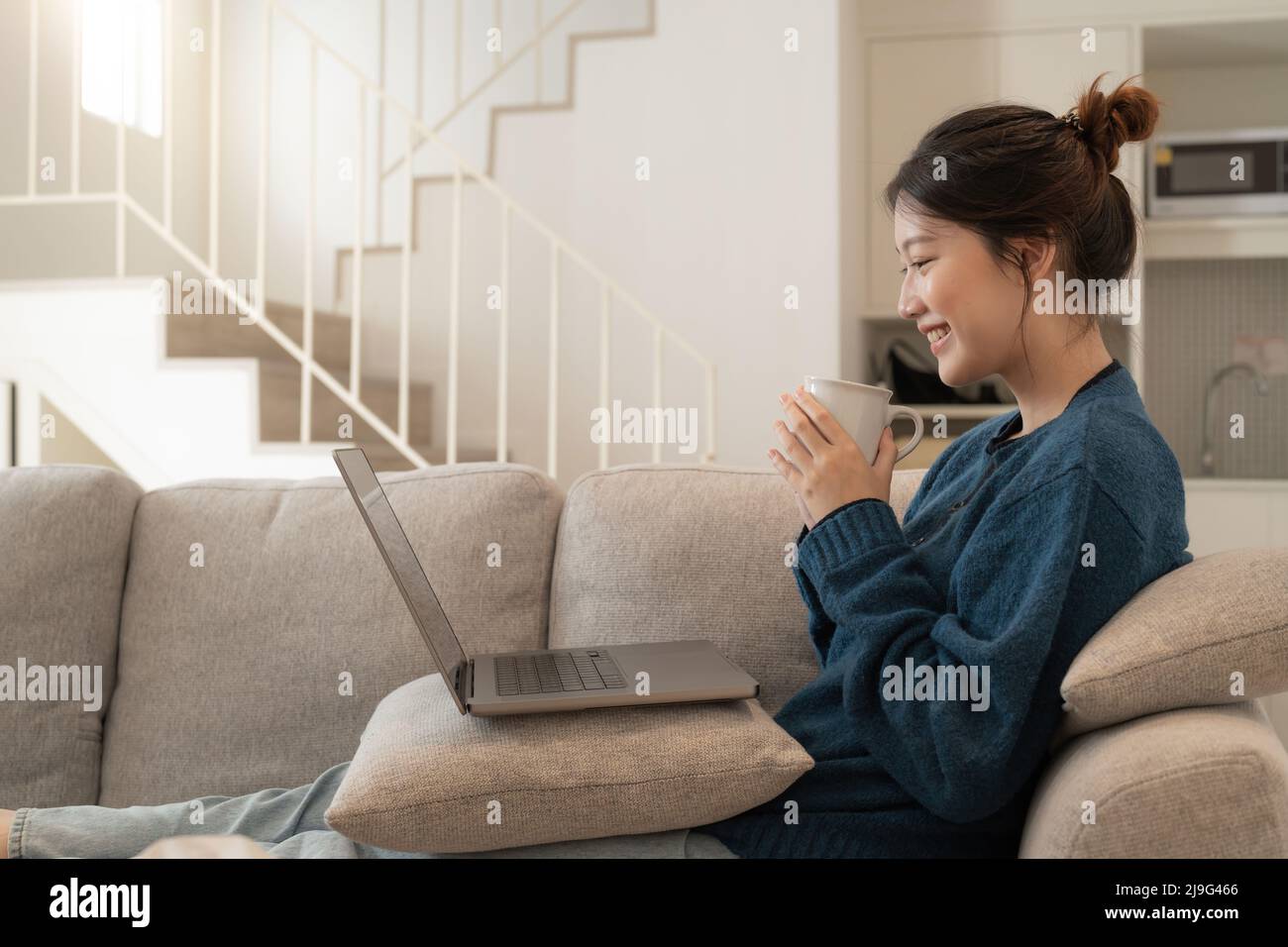 Calm young asian female working at laptop sitting on sofa, happy girl browsing internet or shopping online during sunny weekend at home, relaxing on Stock Photo