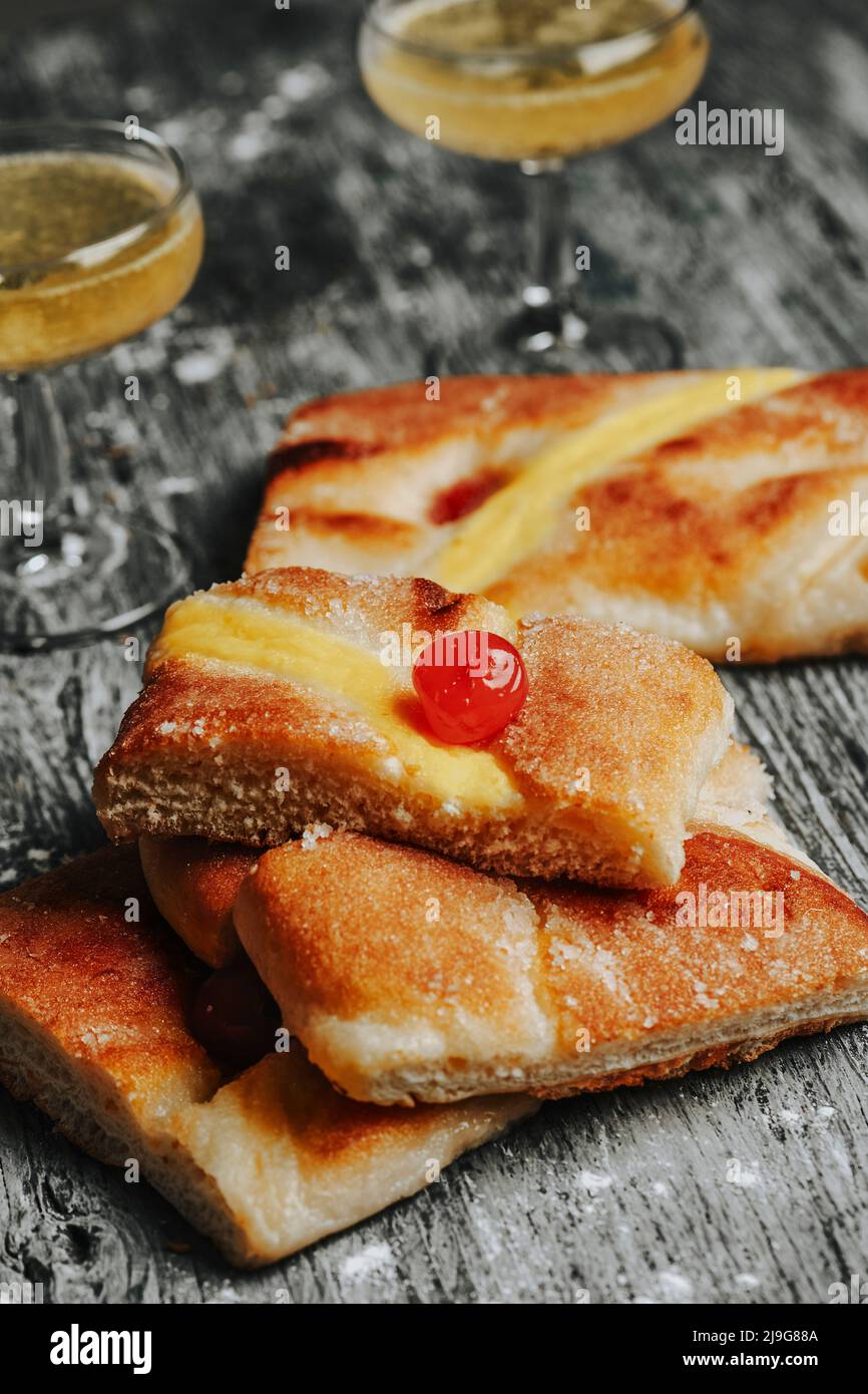 closeup of some pieces of coca de sant joan, a sweet flat cake from catalonia, spain, typically eaten on saint johns eve, and some glasses with catala Stock Photo