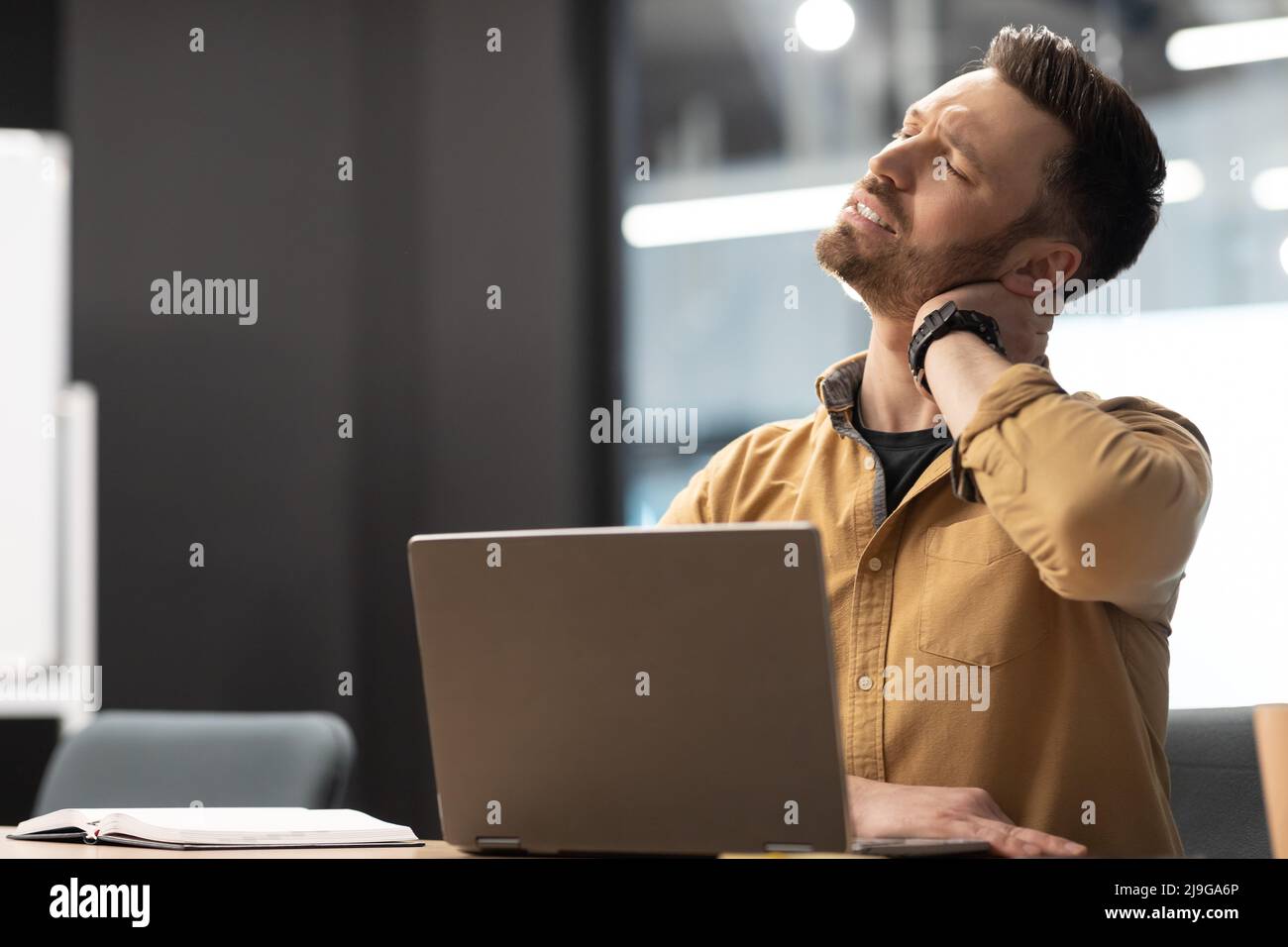 Businessman Touching Neck Suffering From Pain Using Laptop In Office Stock Photo