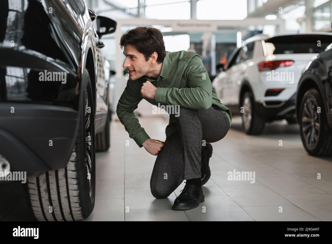Positive young guy checking wheels of new car, buying modern vehicle at