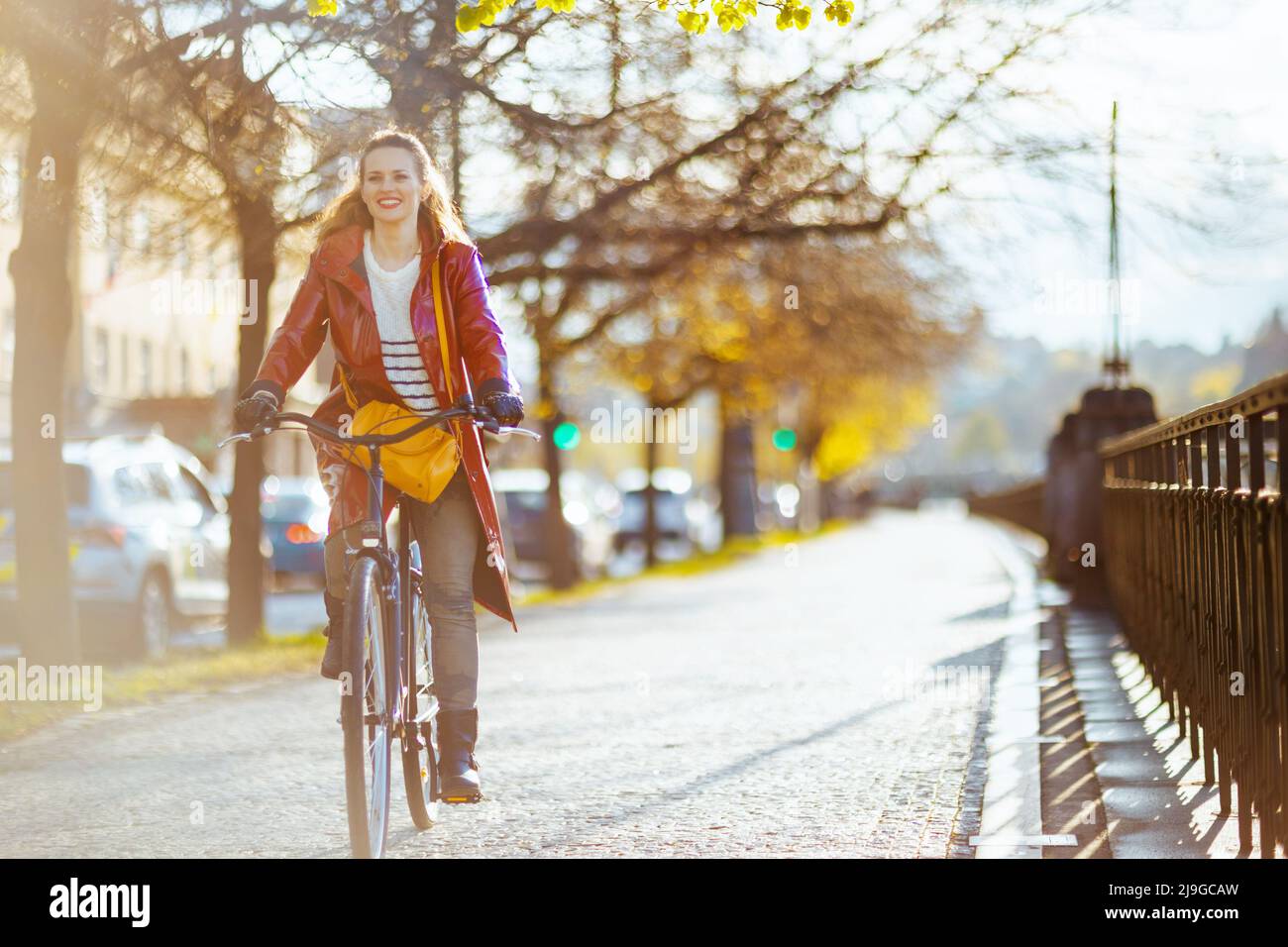 smiling modern woman in red rain coat outside on the city street riding ...