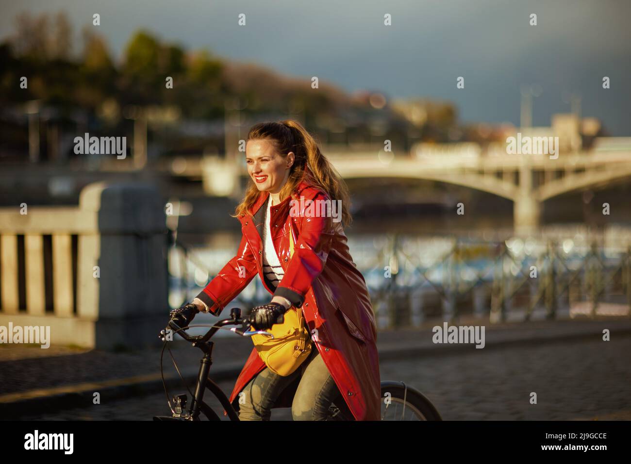 happy stylish woman in red rain coat outdoors on the city street riding ...