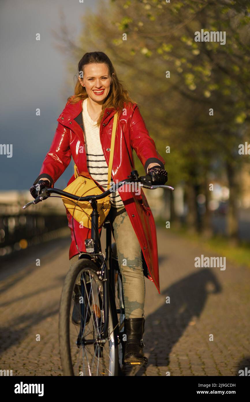happy stylish 40 years old woman in red rain coat outdoors on the city ...