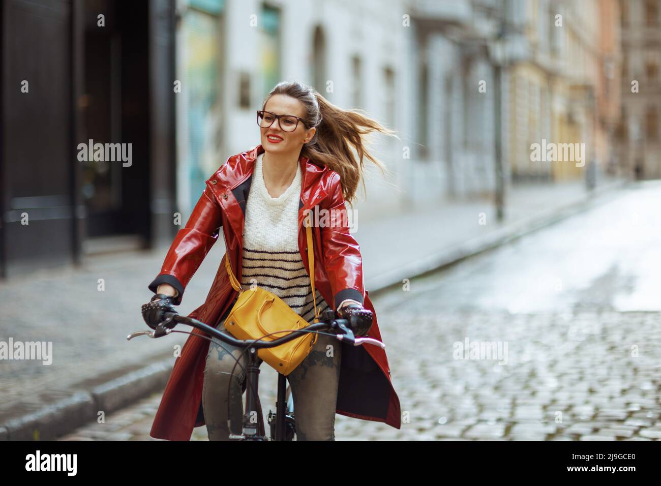 happy stylish woman in red rain coat outdoors on the city street riding ...