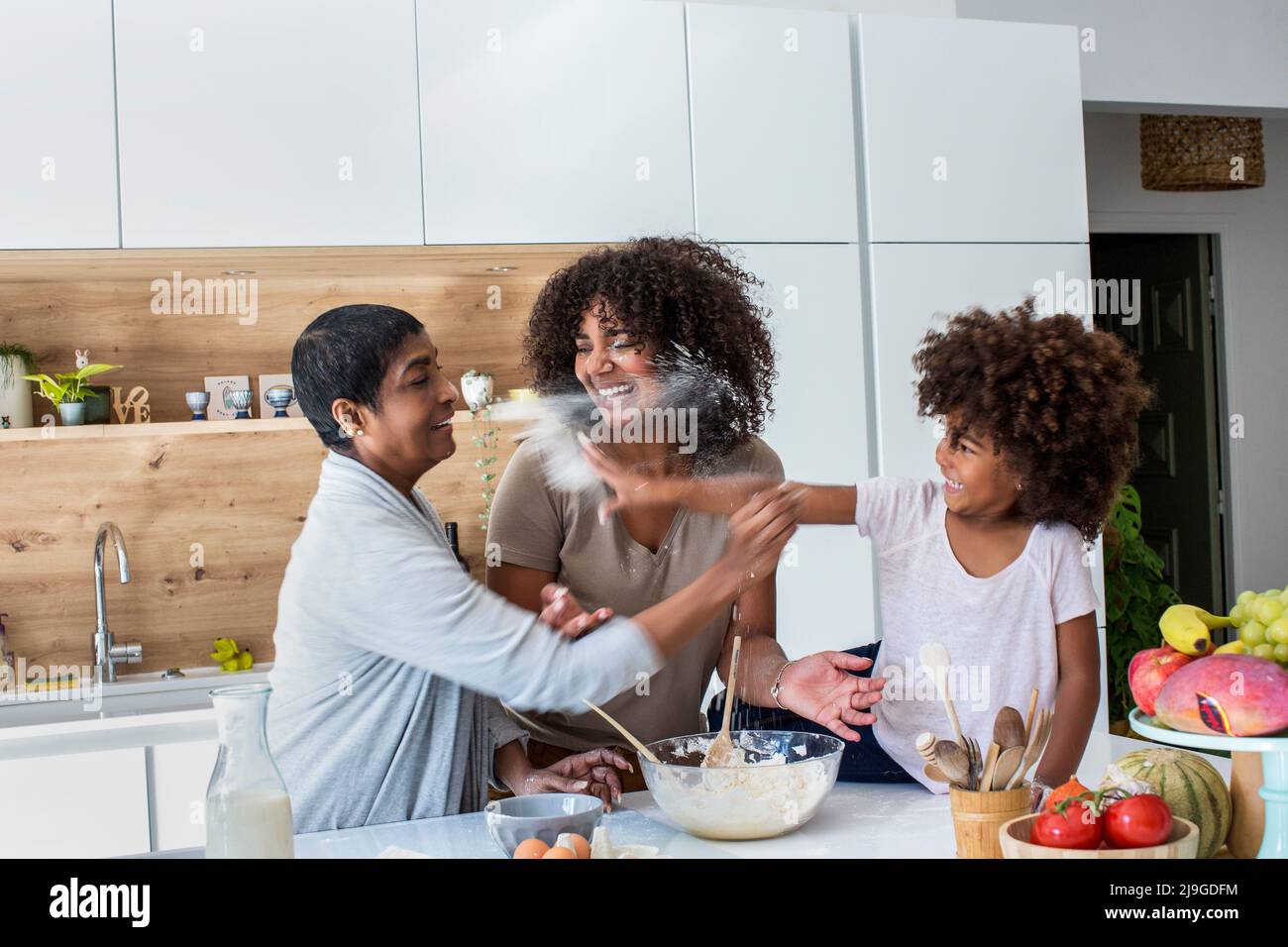 Multi-generation family sprinkling flour in kitchen while preparing cookies Stock Photo