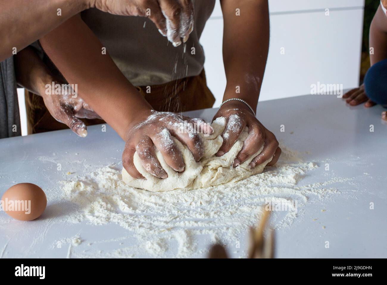 Daughter-in-law kneading dough while mother-in-law sprinkling flour Stock Photo