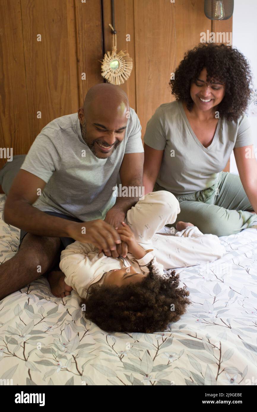 Happy parents playing with daughter on bed Stock Photo