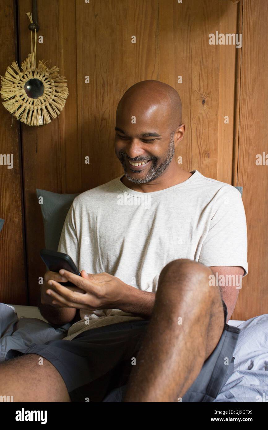 Man using smart phone while sitting in bedroom Stock Photo