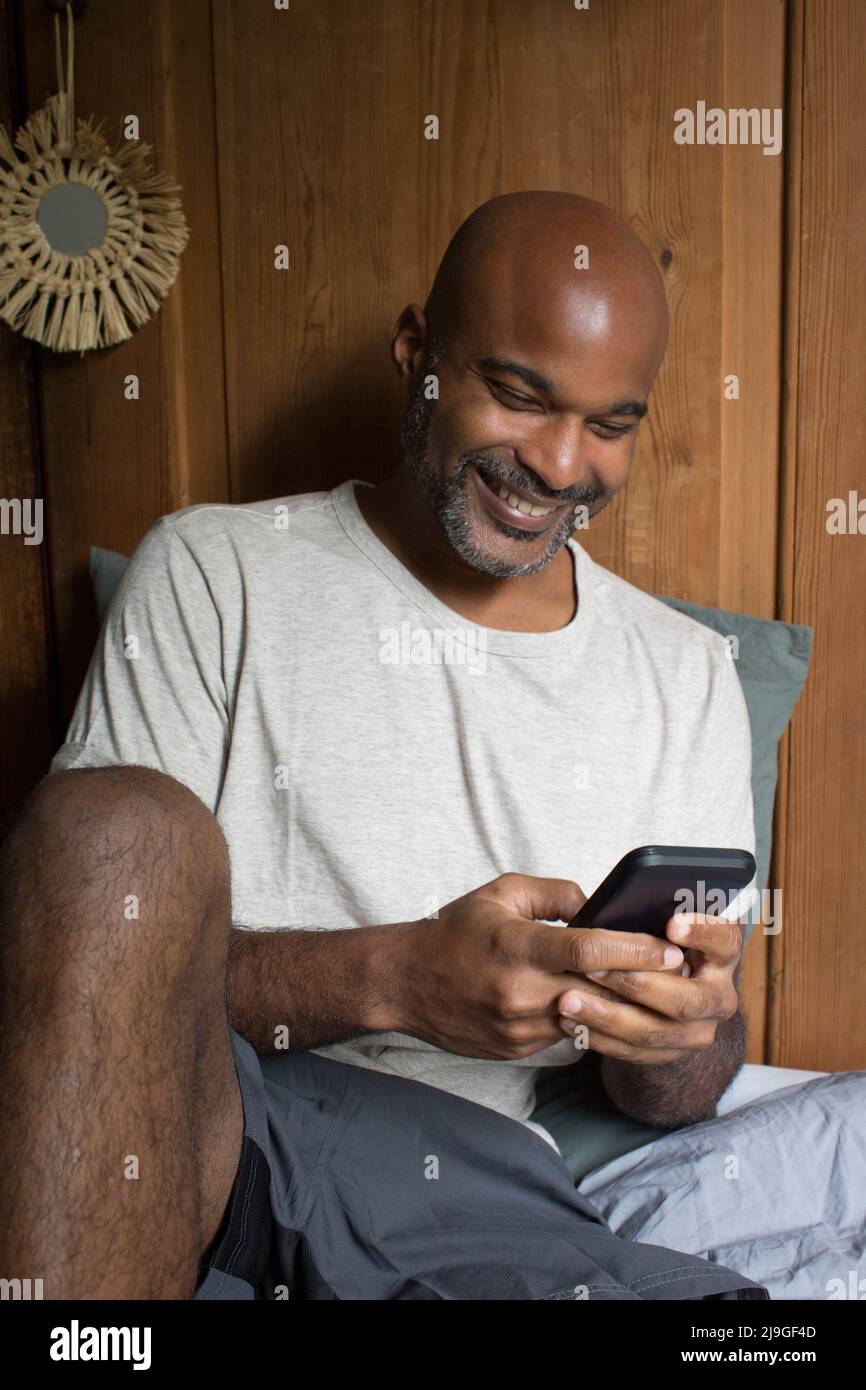 Man using smart phone while sitting in bedroom Stock Photo