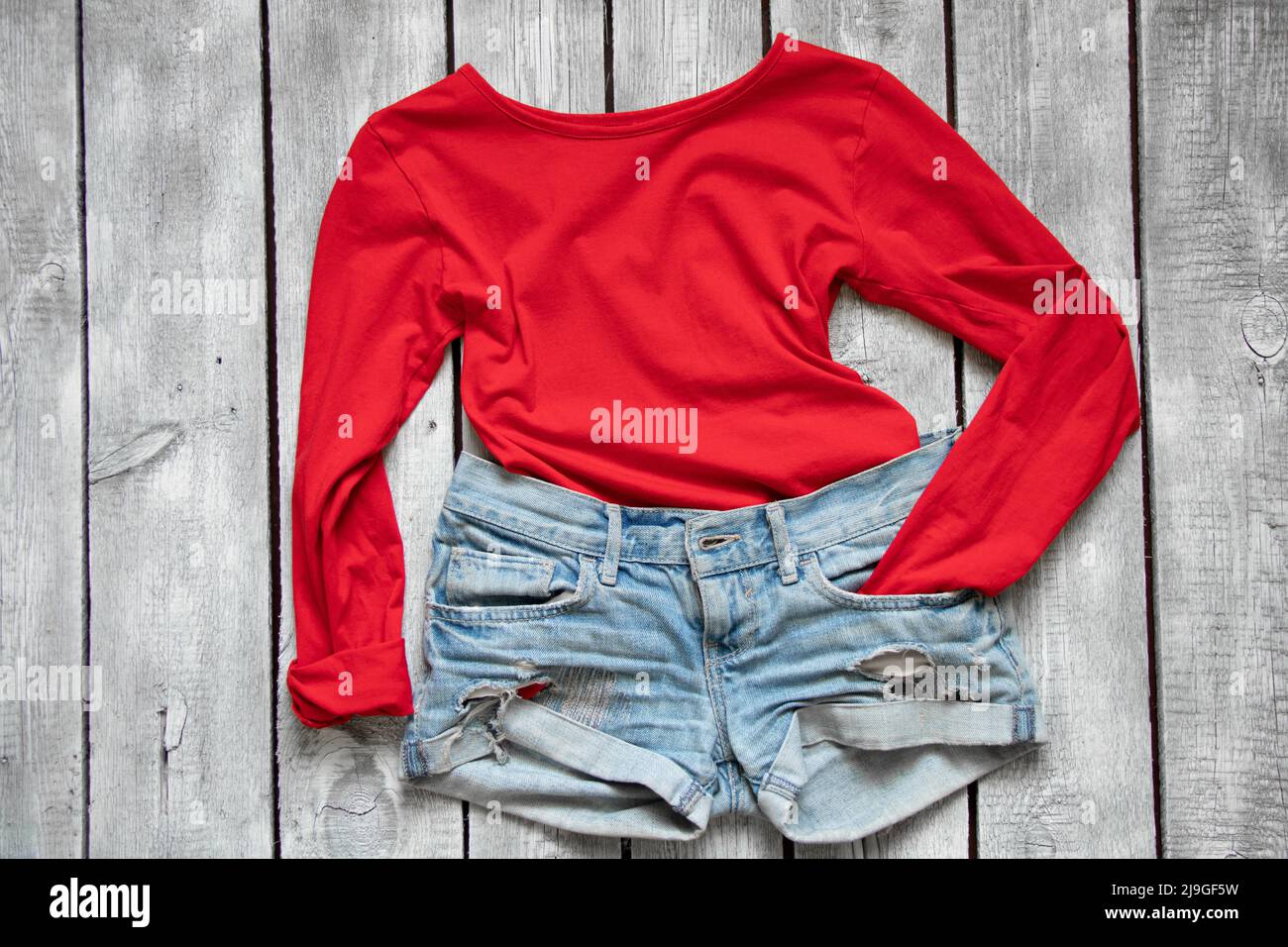red jacket and denim shorts lie on a white wooden table, women's clothing on the table Stock Photo