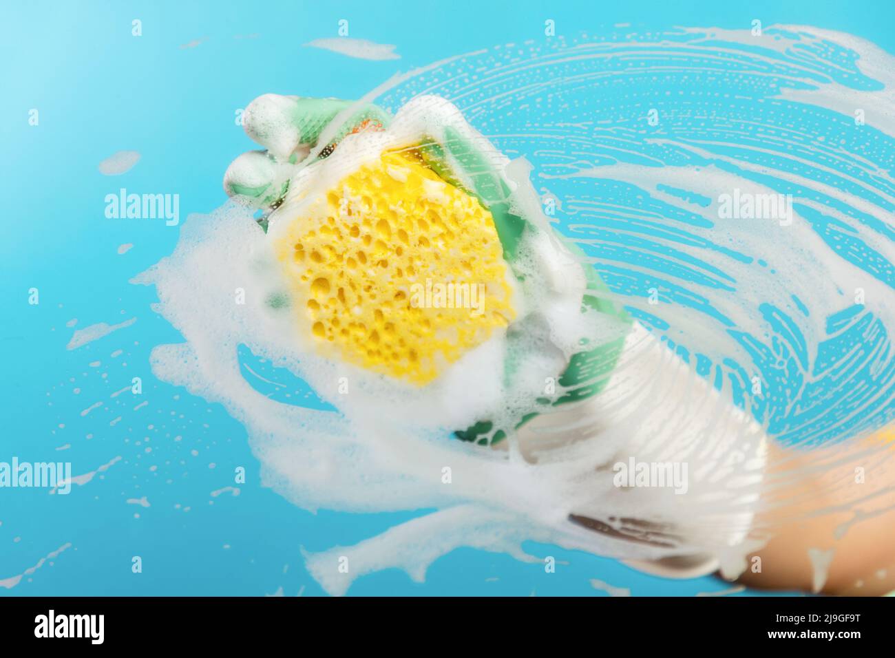 Hand in rubber gloves wipes the glass with a yellow foam sponge. Light