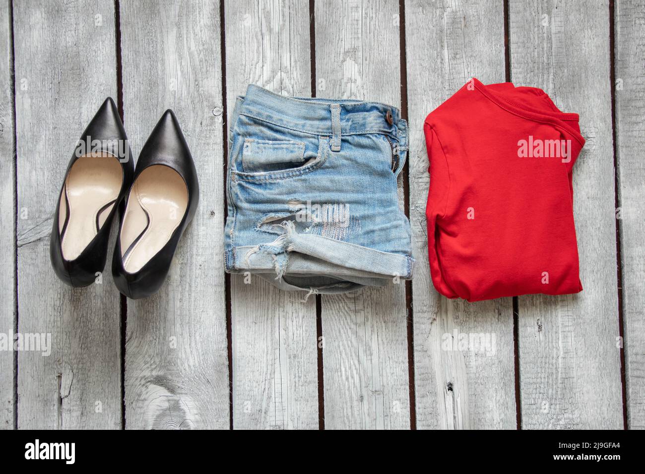 red jacket denim shorts and black leather shoes on a white wooden table, women's clothing on the table Stock Photo