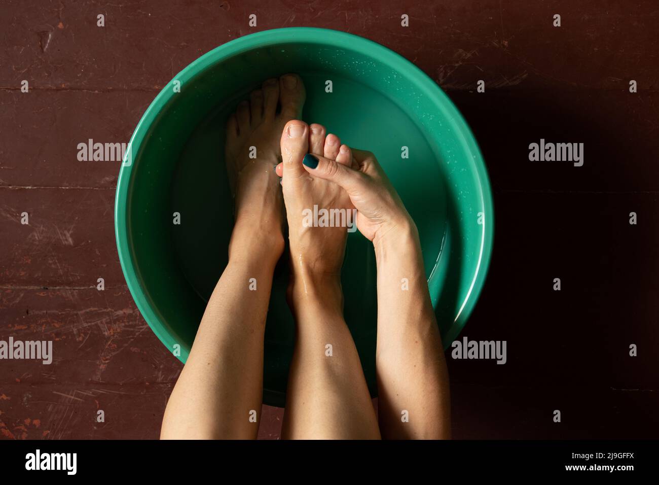 girl washes her feet in a green bowl on the wooden floor of the house, foot care, wash feet